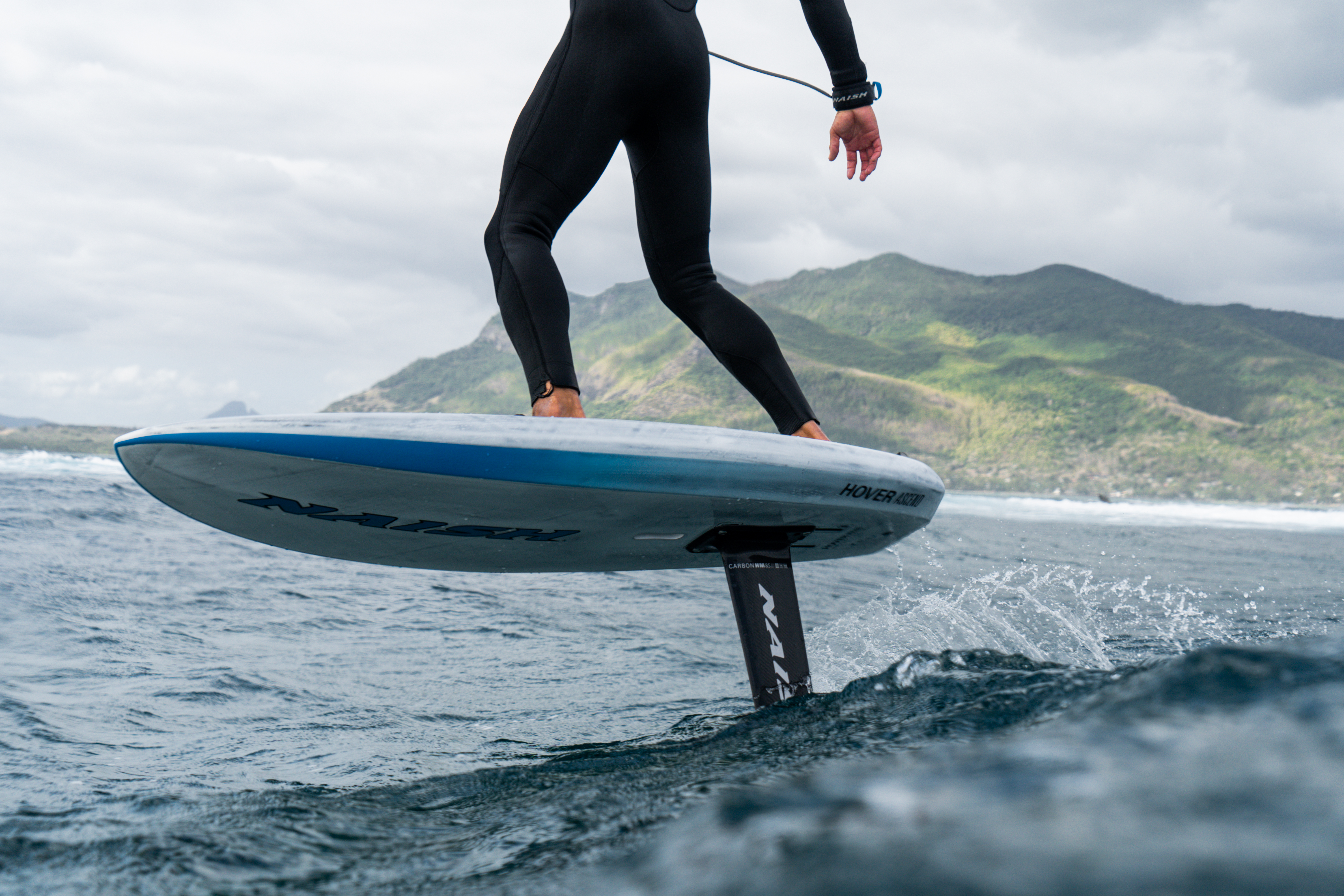 Rider en vol au-dessus de l'eau avec planche foil Naish en session de wing foil