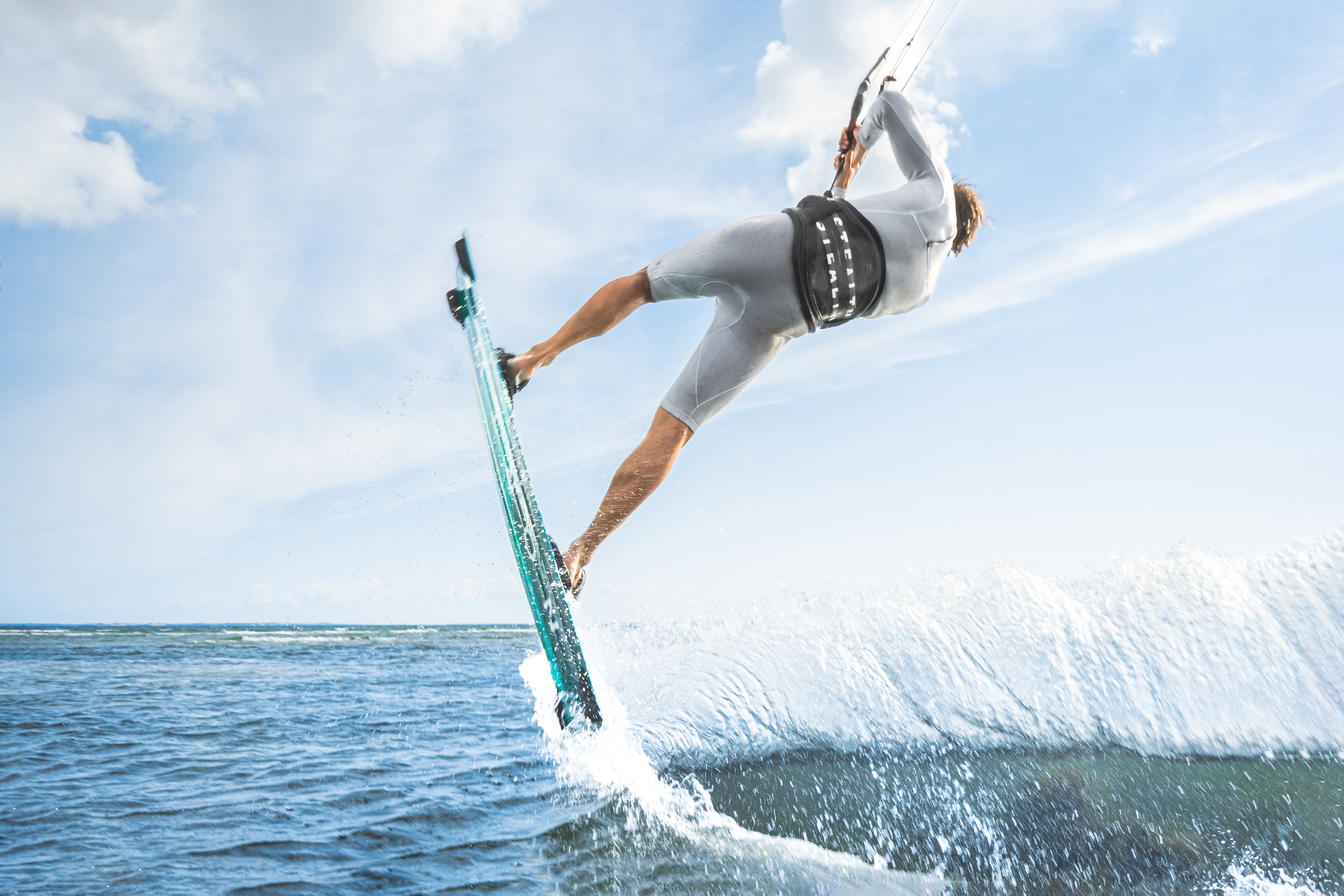 Kitesurfista experimentado realizando una maniobra acrobática en el mar con cielo azul y olas espectaculares.