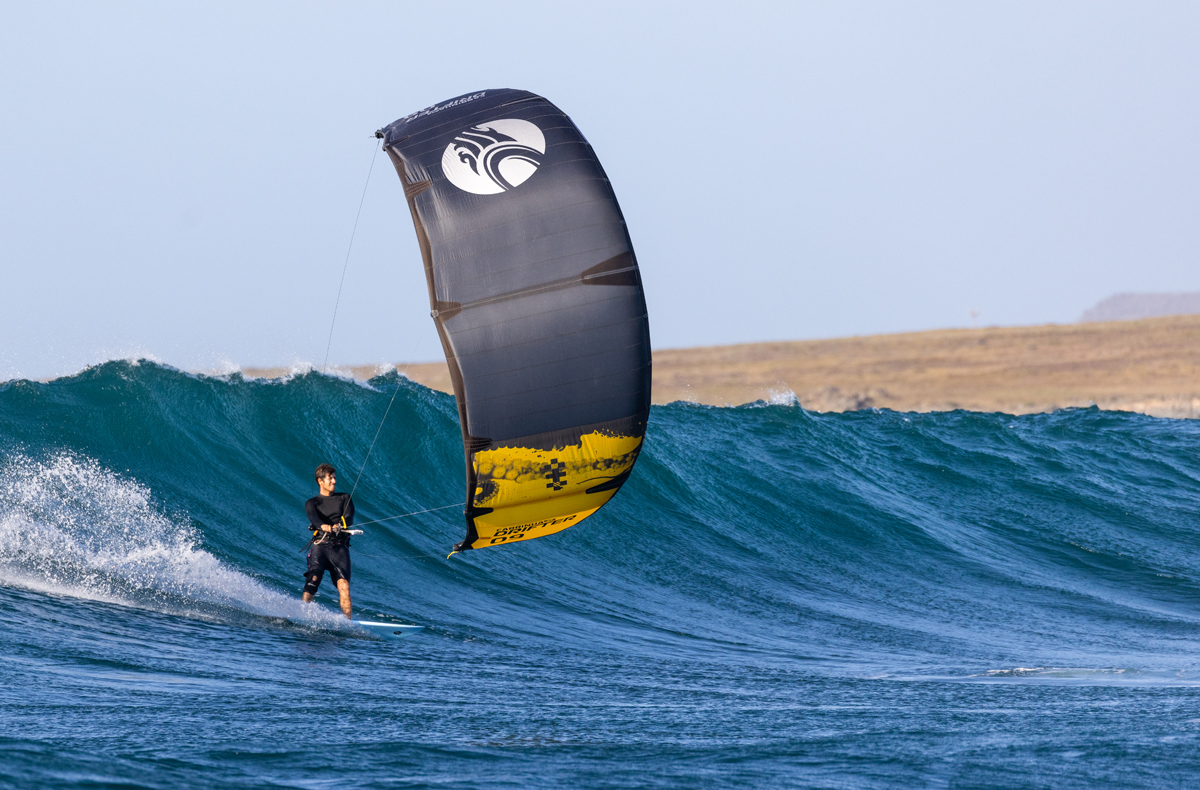 Kitesurfer con vela nera e gialla naviga su un'onda alta in mare aperto.