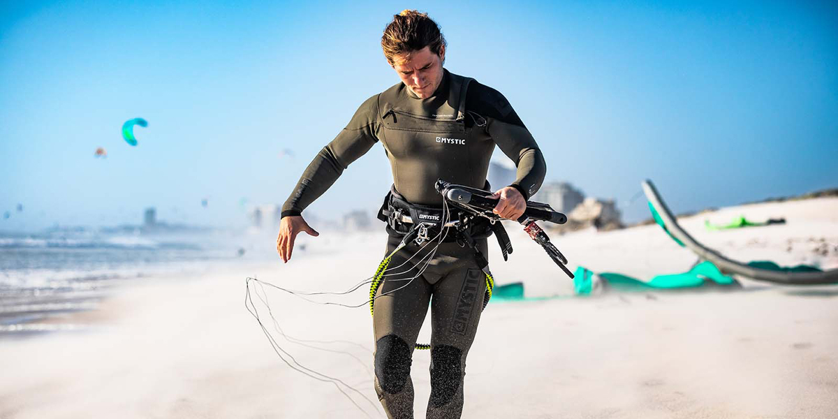 man in kitesurf wetsuit with gear on the beach