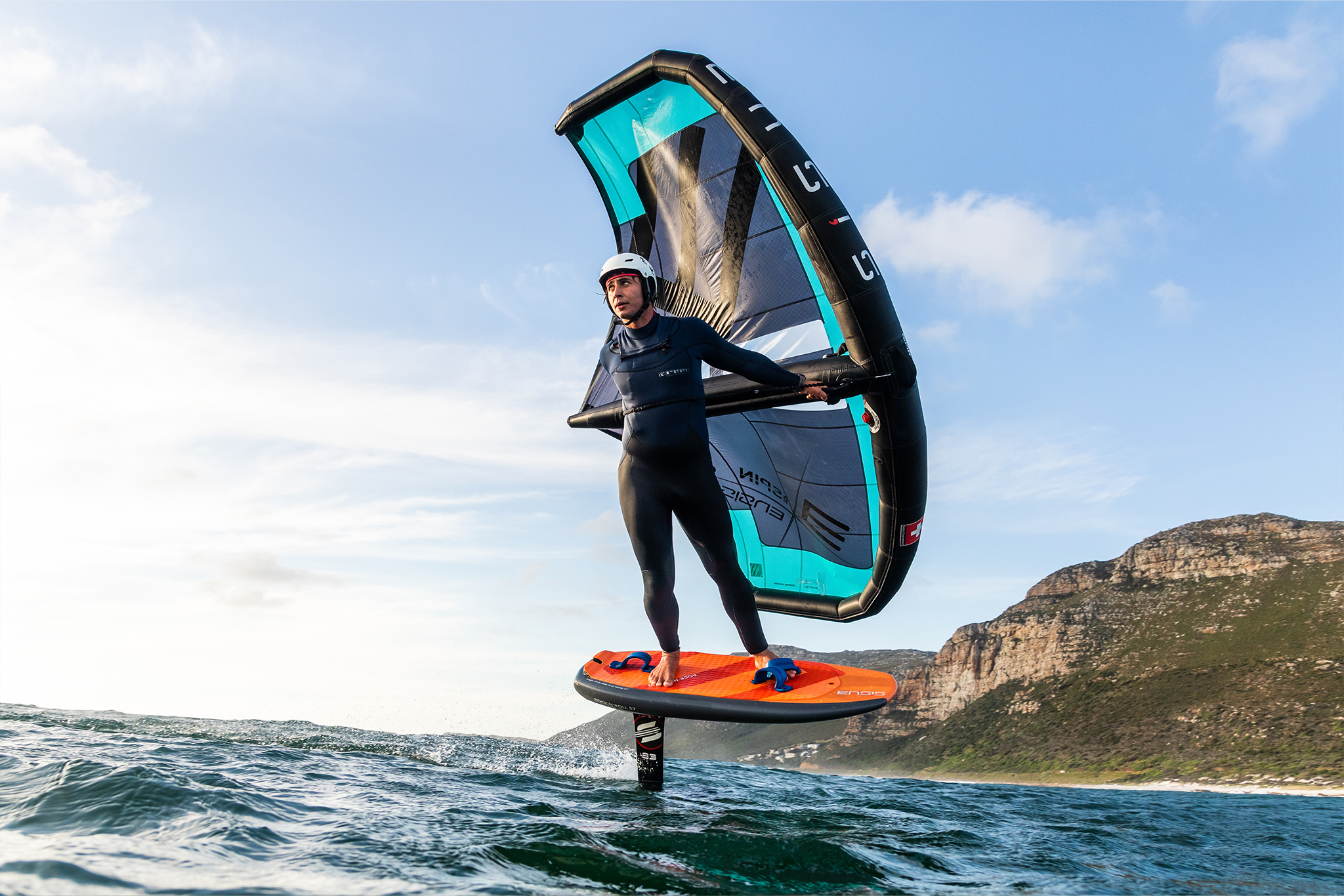 Rider with a blue and black wing foil lifting the board above the water.